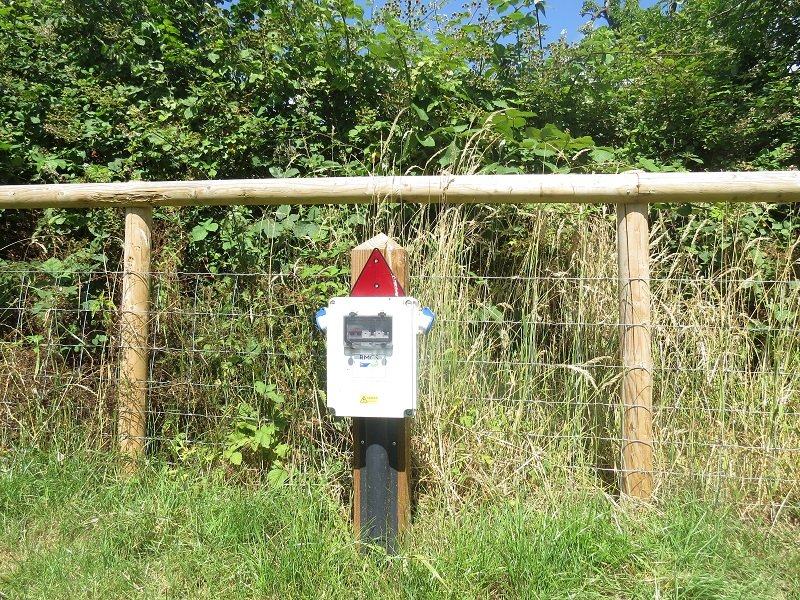 An electric hook-up point mounted on a post by the hedge.