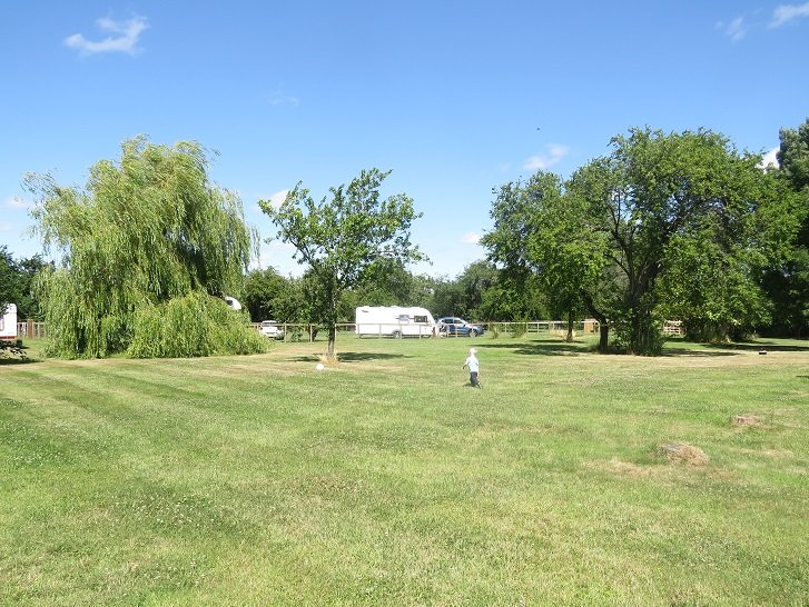 The site in summer, caravans spread out across the open grass field.